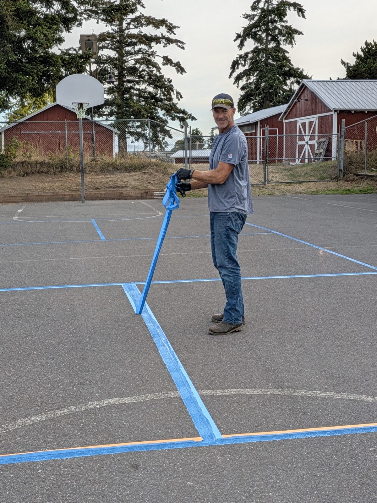 David Kane pulling up painter's tape after painting pickleball lines on the elementary school court